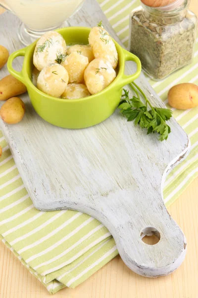 Tender young potatoes with sour cream and herbs in pan on wooden board on table close-up — Stock Photo, Image