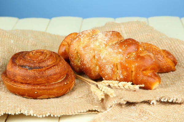 Composition with buns in wicker basket, on wooden table, on color background — Stock Photo, Image