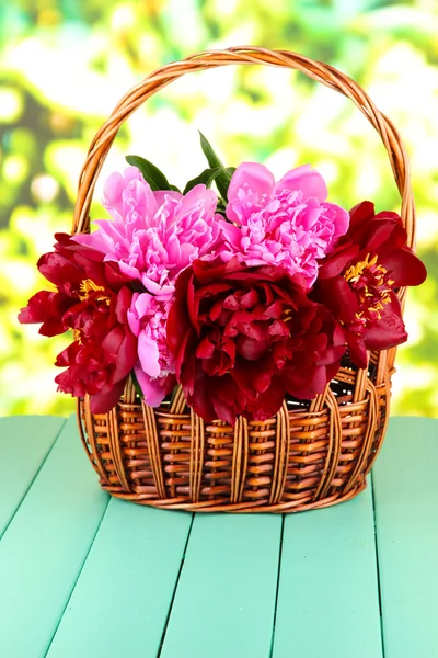 Piękne piwonie w wiklinowym koszu na stole na jasnym tle — Zdjęcie stockowe