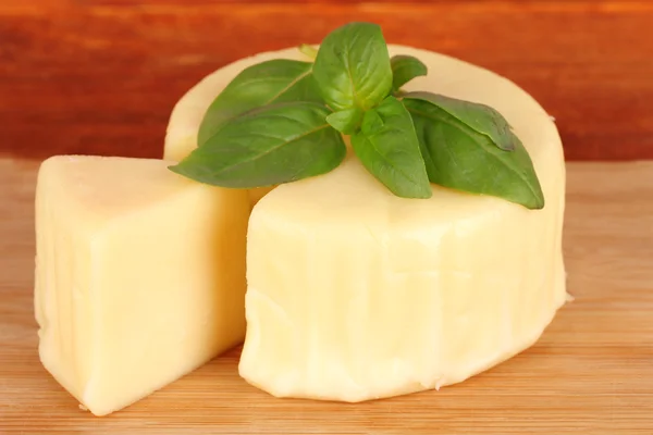 Cheese mozzarella and basil on cutting board on wooden background — Stock Photo, Image