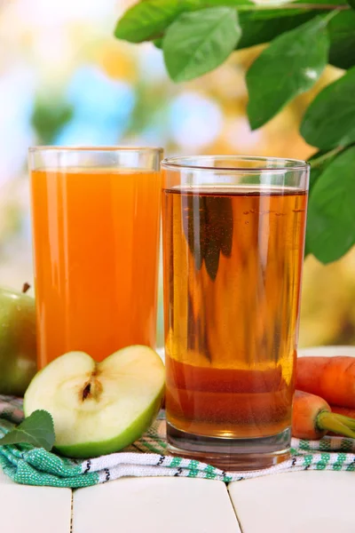 Verres de jus, pommes et carottes sur table en bois blanc, sur fond vert — Photo