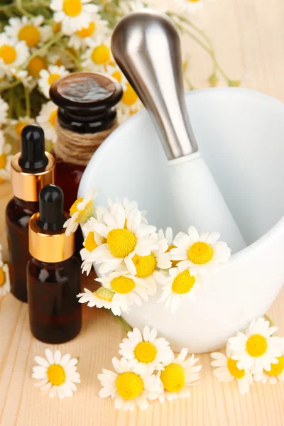 Aceite esencial y flores de manzanilla en mortero sobre mesa de madera —  Fotos de Stock