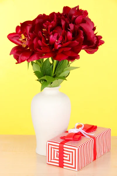 Beautiful peonies in vase on table on yellow background — Stock Photo, Image