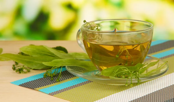 Copa de vidrio de té con tilo en servilleta sobre mesa de madera sobre fondo natural —  Fotos de Stock