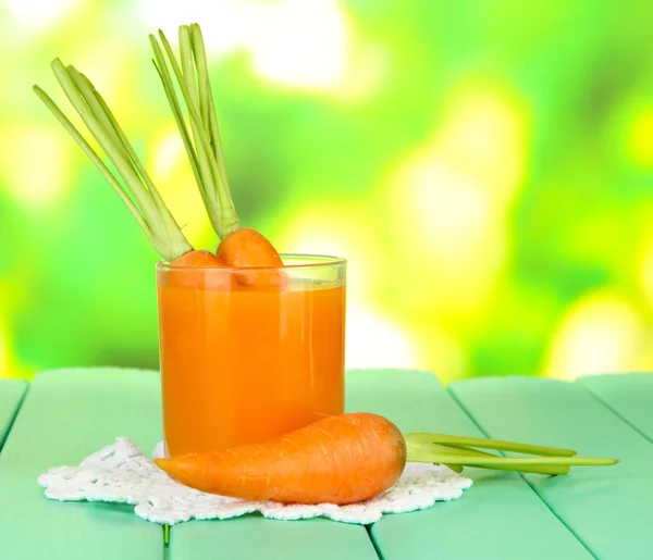 Verre de jus de carotte, sur table en bois de couleur sur fond lumineux — Photo