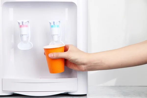 Woman filling cup at water cooler — Stock Photo, Image