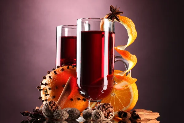 Vinho quente nos copos, tempero e laranja no fundo roxo — Fotografia de Stock