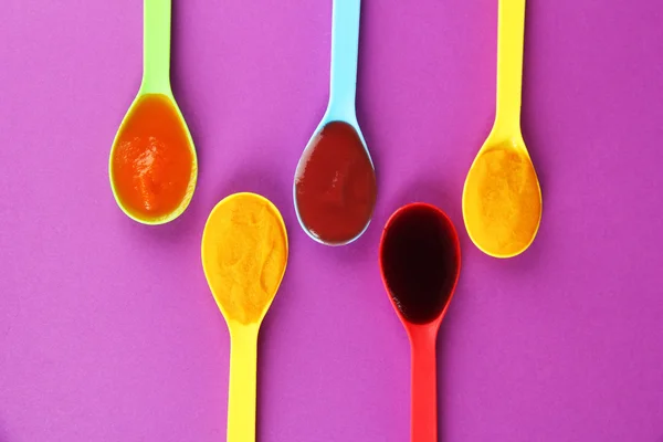 Baby puree in spoons on purple background — Stock Photo, Image