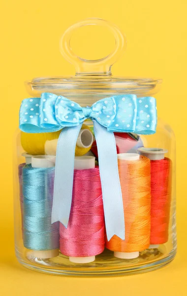 Glass jar containing various colored thread on yellow background — Stock Photo, Image