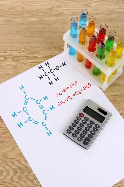 Пробирки с красочными жидкостями и формулами на столе — стоковое фото