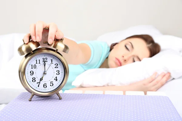 Beautiful young woman sleeping on bed with alarm clock in bedroom — Stock Photo, Image