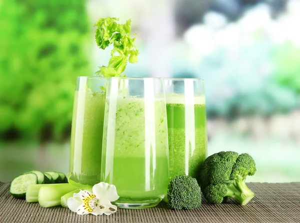 Bicchieri di succo vegetale, su tappetino di bambù, su fondo verde — Foto Stock