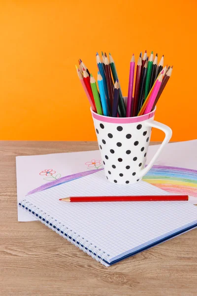 Buntstifte in Tasse auf Tisch auf orangefarbenem Hintergrund — Stockfoto