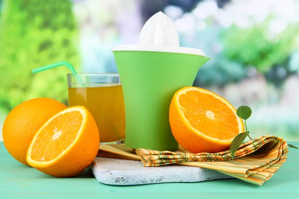 Imprensa de citrinos, copo de suco e laranjas maduras na mesa de madeira verde — Fotografia de Stock