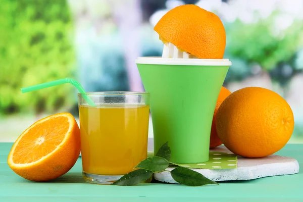 Citrus press, glass of juice and ripe oranges on green wooden table — Stock Photo, Image