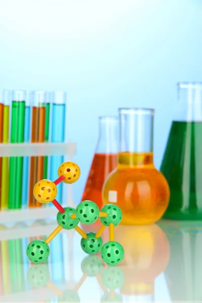 Molekülmodell und Reagenzgläser mit bunten Flüssigkeiten auf blauem Hintergrund — Stockfoto