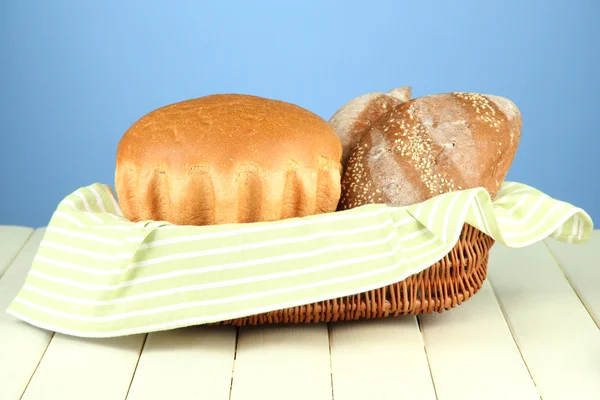 Bread in wicker basket, on wooden table, on color background — Stock Photo, Image