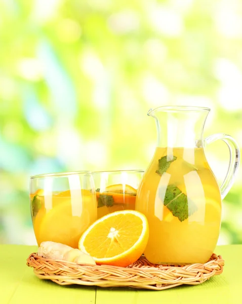 Limonata arancione in brocca e bicchieri su tavolo in legno su sfondo naturale — Foto Stock