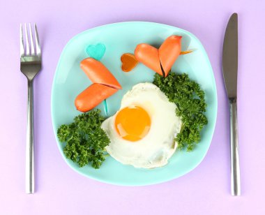 Sausages in form of hearts, scrambled eggs and parsley, on color plate, on color background