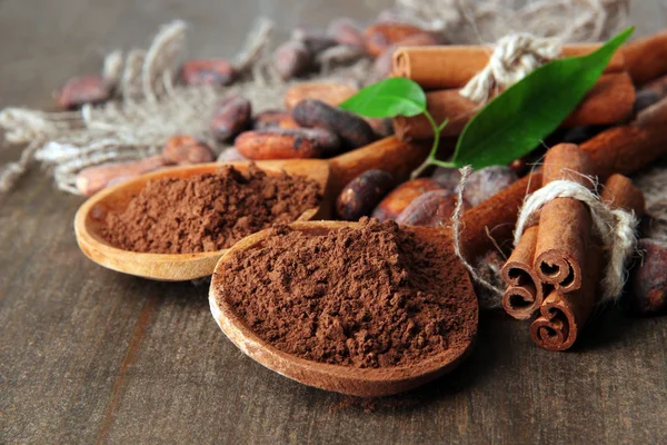 Poudre de cacao dans des cuillères et fèves de cacao sur fond en bois — Photo