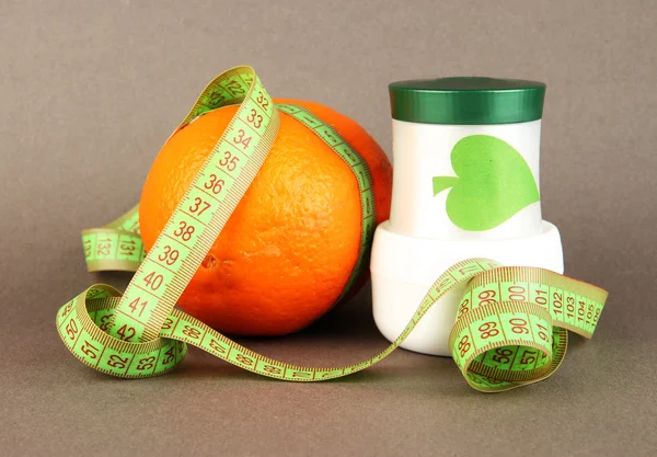 Orange with measuring tape and body cream, on color background — Stock Photo, Image