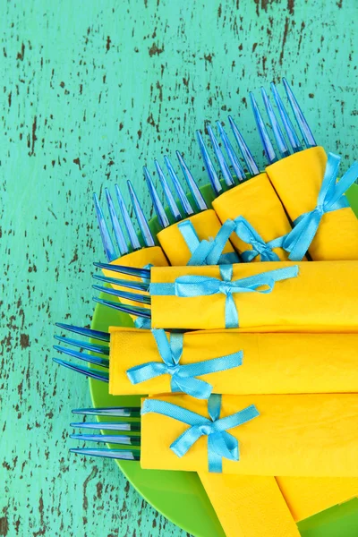 Tenedores de plástico azul envueltos en servilletas de papel amarillo, sobre fondo de madera de color —  Fotos de Stock