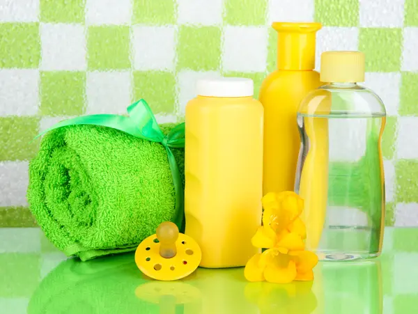 Cosméticos para bebés y toalla en el baño sobre fondo de pared de azulejos verdes —  Fotos de Stock
