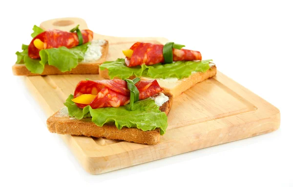 Salami rolls with paprika pieces inside, on roasted bread, on wooden board, isolated on white — Stock Photo, Image