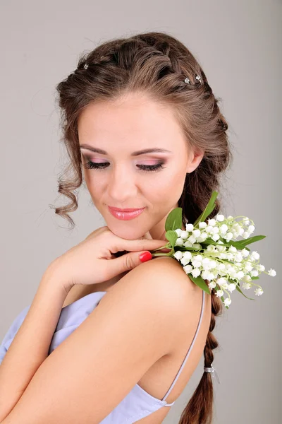 Mujer joven con hermoso peinado y flores, sobre fondo gris — Foto de Stock