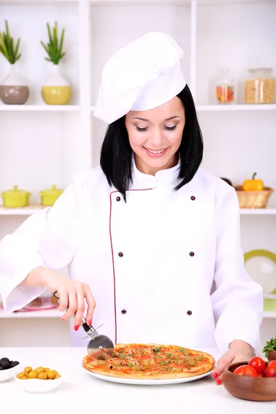 Hermosa chica jefe de cocina con pizza en el fondo de la cocina — Foto de Stock