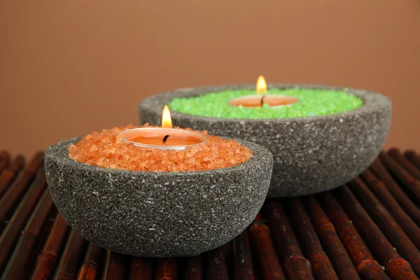 Candles in stone bowls with marine salt, on bamboo mat, on brown background — Stock Photo, Image