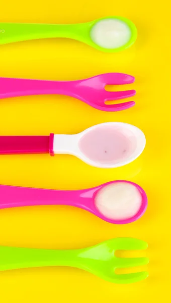 Colheres de cor e garfos para alimentos para bebês no fundo amarelo — Fotografia de Stock