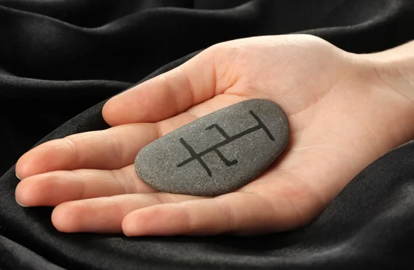 Fortune telling with symbols on stone in hand on black fabric background — Stock Photo, Image