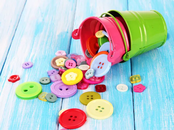 Colorful buttons strewn from buckets on wooden background — Stock Photo, Image