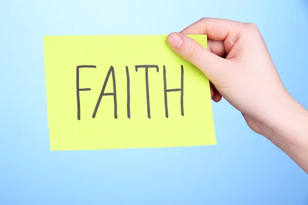 Faith word on piece paper in hand on blue background — Stock Photo, Image