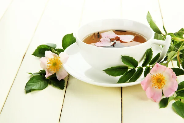 Taza de té de hierbas con flores de rosa de la cadera en mesa de madera blanca —  Fotos de Stock