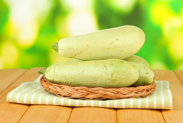 Fresh marrows on wicker mat, on wooden table, on bright background — Stock Photo, Image