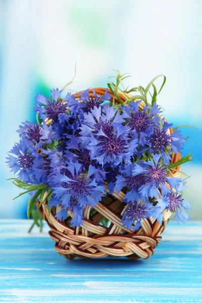 Beautiful bouquet of cornflowers in basket on blue background — Stock Photo, Image