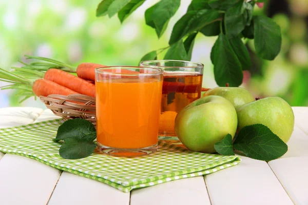 Glasses of juice, apples and carrots on white wooden table, on green background — Stock Photo, Image