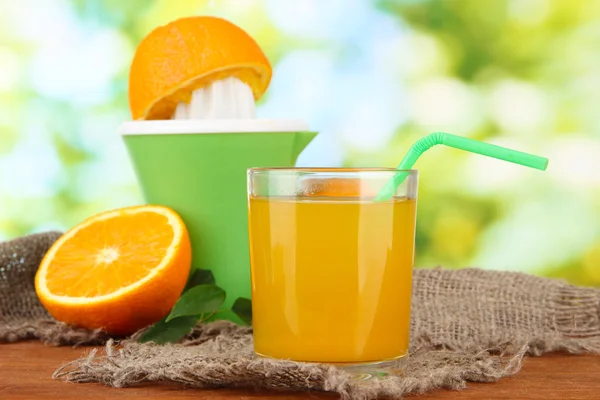 Citrus press, glass of juice and ripe oranges on brown wooden table — Stockfoto