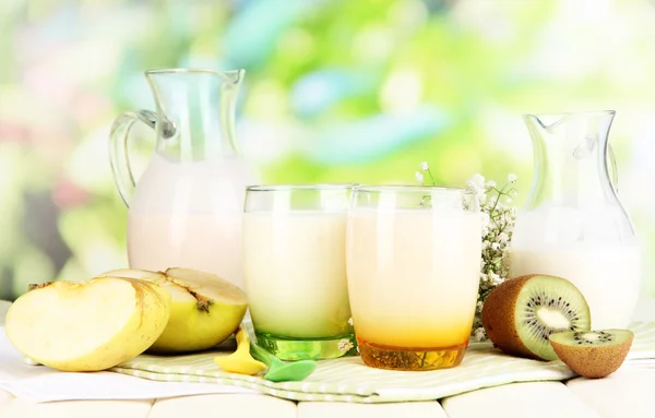 Iogurtes deliciosos com frutas em óculos na mesa de madeira no fundo natural — Fotografia de Stock