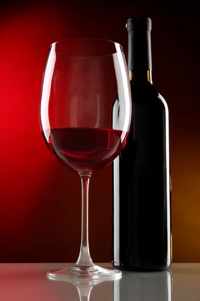 Ποτήρι κρασί με το μπουκάλι σε φωτεινό κόκκινο φόντο — Φωτογραφία Αρχείου