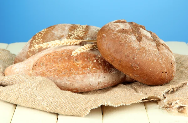 Composition with bread and sackcloth on wooden table, on color background — Stock Photo, Image