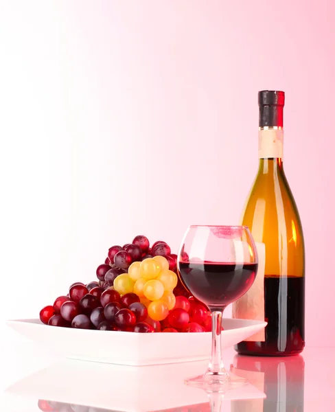 Copo de vinho com marca de batom, uvas e garrafa sobre fundo rosa — Fotografia de Stock