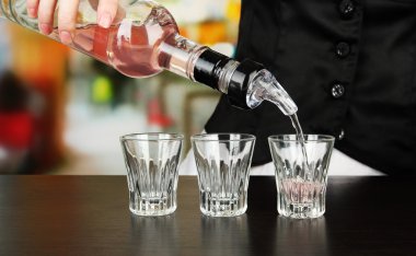Barmen hand with bottle pouring beverage into glasses, on bright background clipart