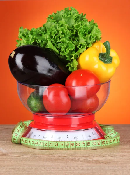Färska grönsaker i skalor på tabellen på orange bakgrund — Stockfoto
