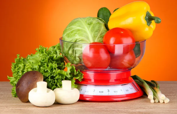 Fresh vegetables in scales on table on orange background — Stock Photo, Image