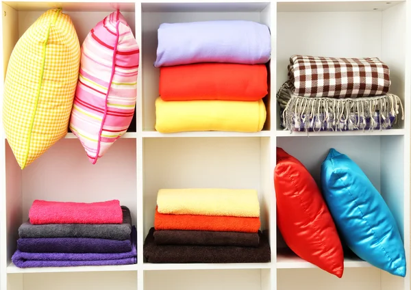 Bright pillows, towels and plaids on shelves, isolated on white — Stock Photo, Image