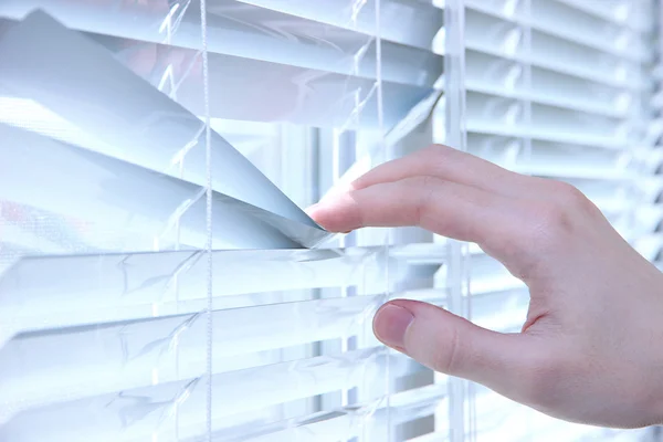 Someone looking out of window opening blinds — Stock Photo, Image