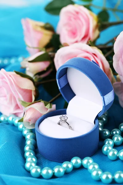 Róża i pierścionek zaręczynowy na niebieski tkaniny — Zdjęcie stockowe